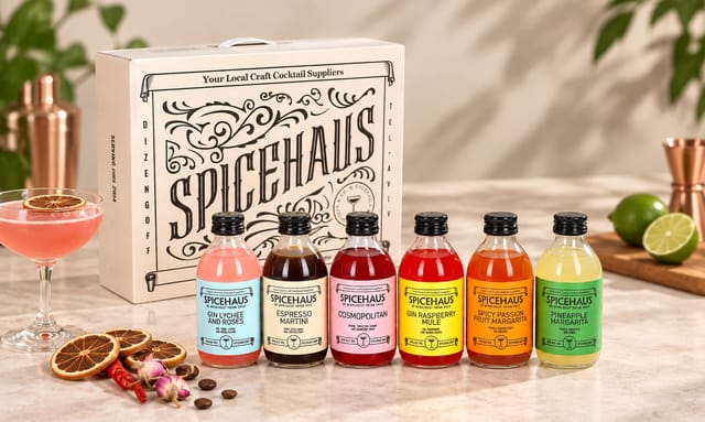 מארז קוקטיילים של Spicehaus הכולל מארז לבן, שישה בקבוקי קוקטייל בטעמים שונים וחוברת, לצד פירות ותבלינים מיובשים על רקע לבן ונקי.